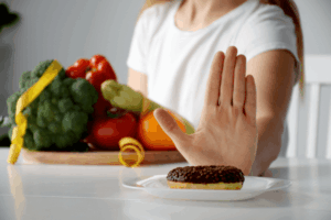 Woman on a diet pushing away a donut to maintain healthy eating habits.